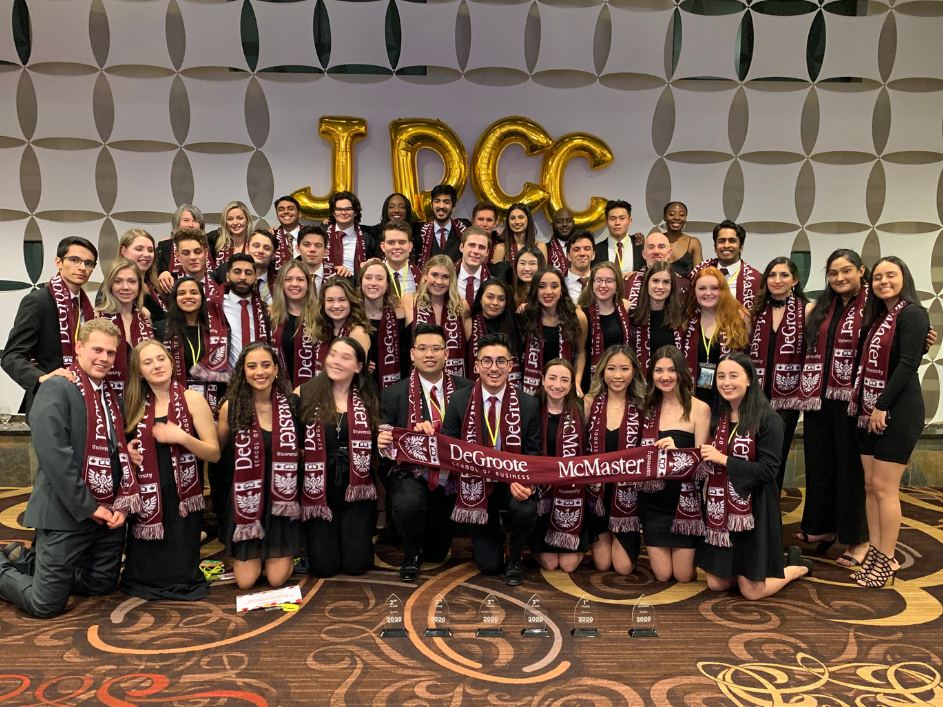 Undergraduate-Commerce-Courses. A gathering of individuals standing together, captured in a photograph, positioned before an expansive banner. JDCC Competition crew.
