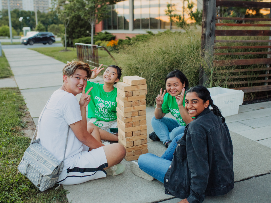 Undergraduate-Contact-Us. A group of four young individuals can be observed sitting on the sidewalk, partaking in Jenga.