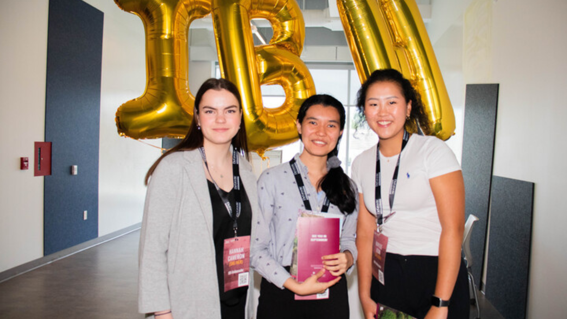 Undergraduate-IBH. Three female individuals posing adjacent to a sizable balloon featuring the alphanumeric symbol 
