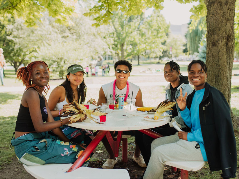 Undergraduate-Supplemental-Application. Seated at a picnic table amidst a peaceful McMaster University campus, five young students are seen, displaying a relaxed demeanor as they engage in conversation.